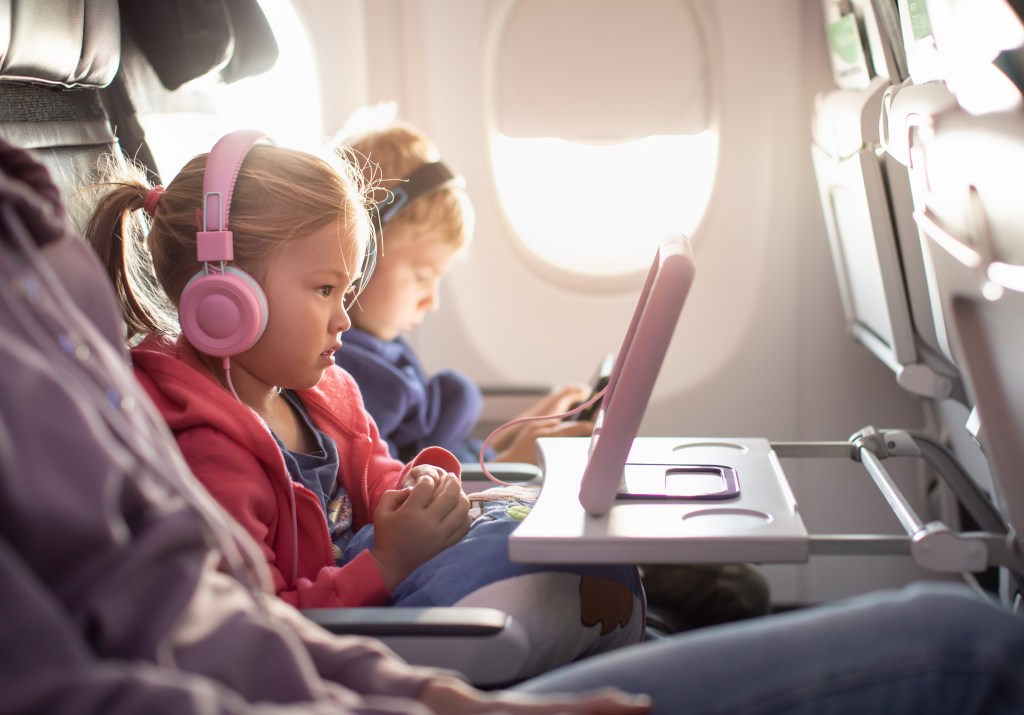 Adorable little boy and girl sitting near airplane window watching video during a flight